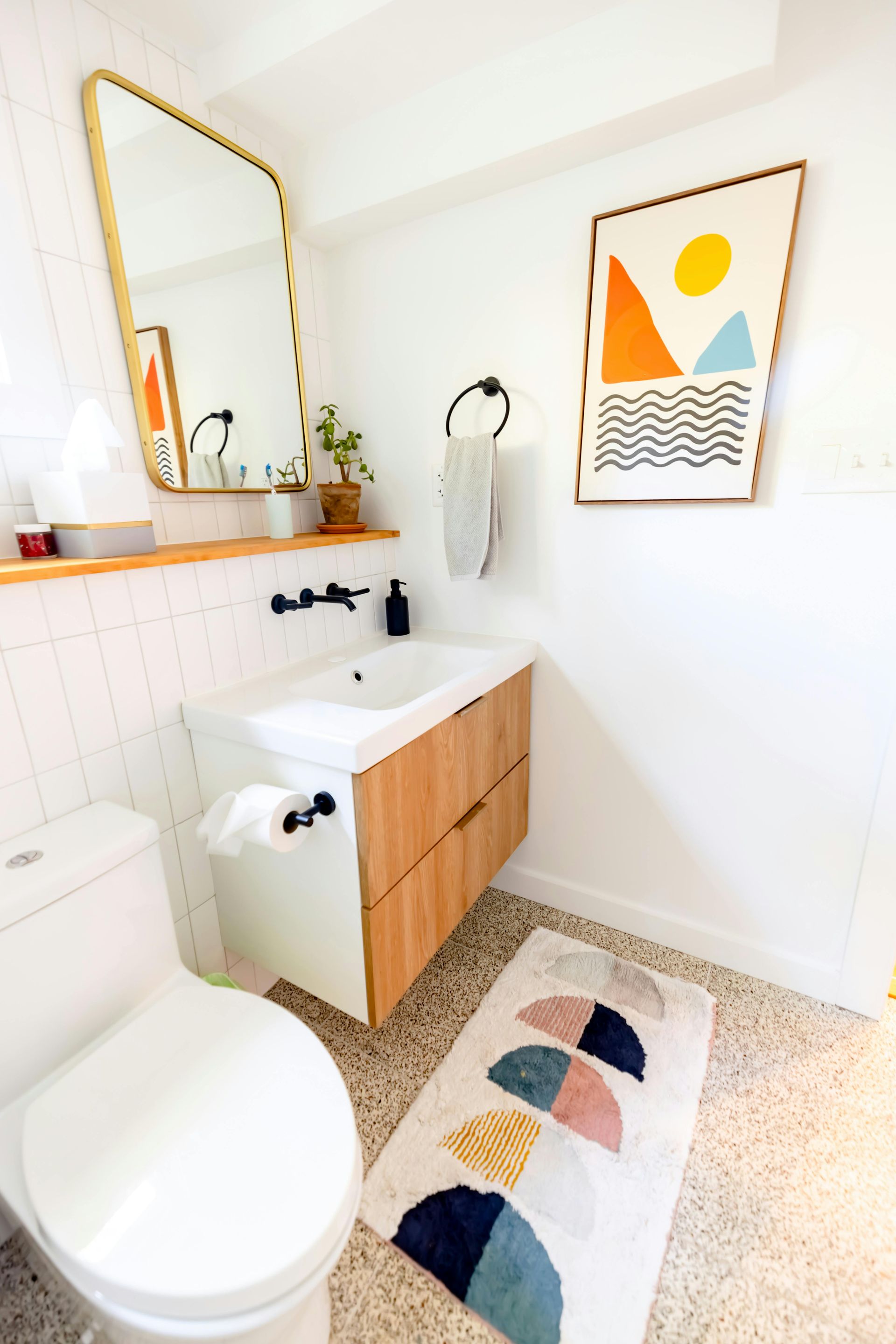 A bathroom with a toilet , sink , mirror and rug.