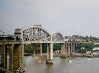 Bridge arches over water with boats, stone towers supporting it, small houses on the shore.