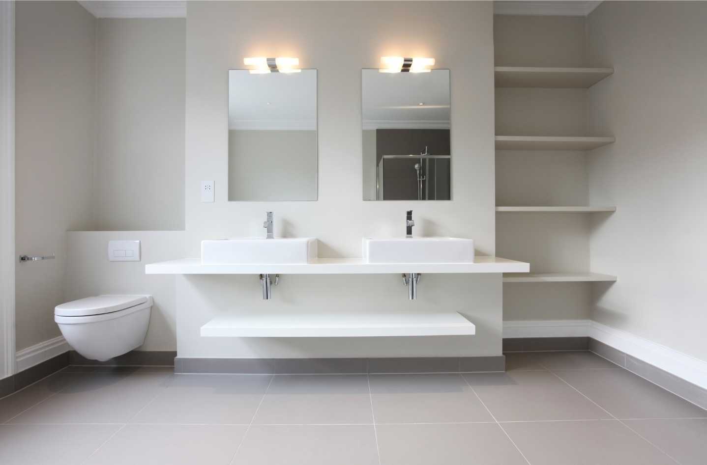 A bathroom with two sinks , a toilet and shelves.