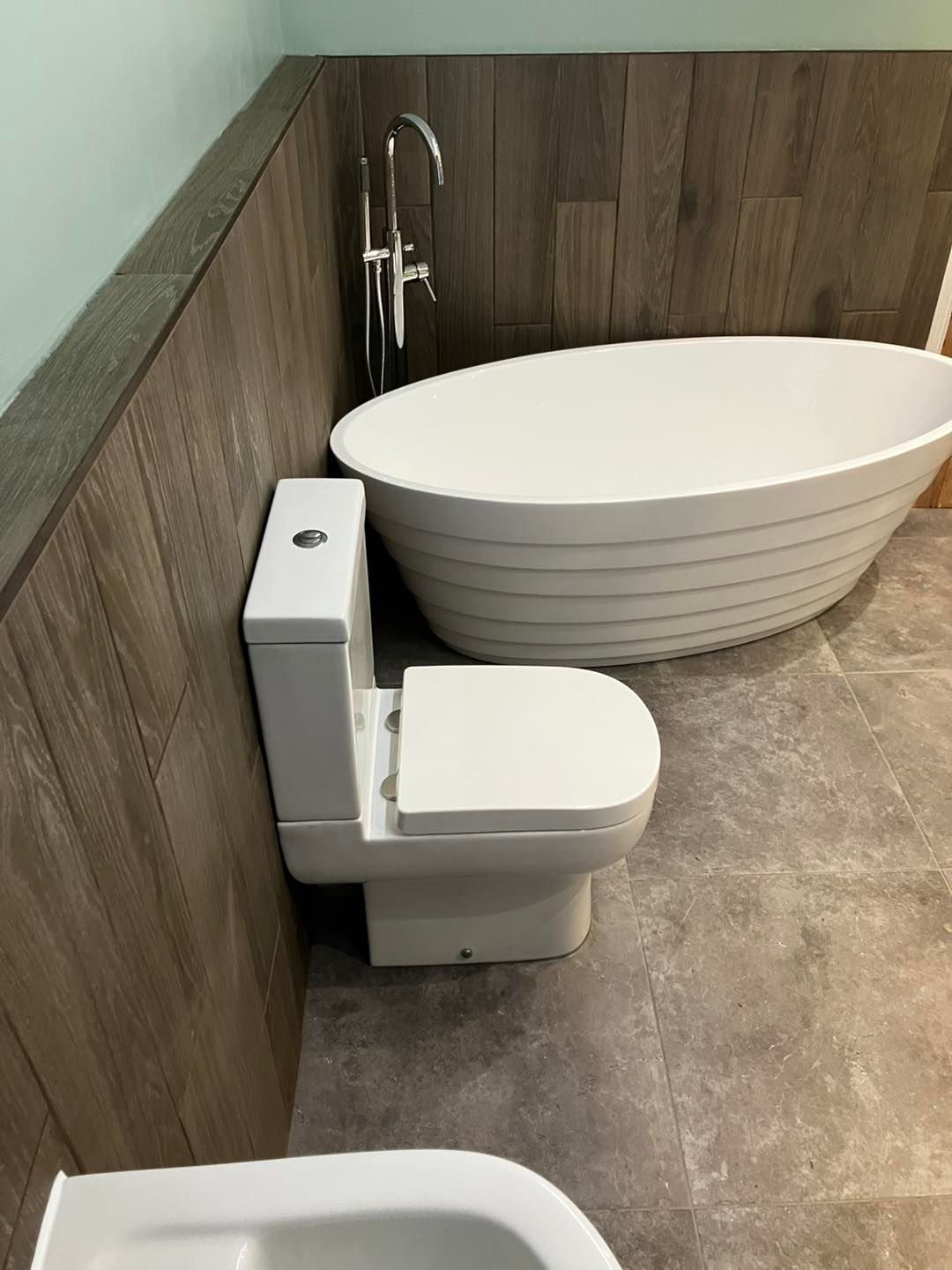 Modern bathroom with white toilet and oval freestanding tub beside wood-paneled walls
