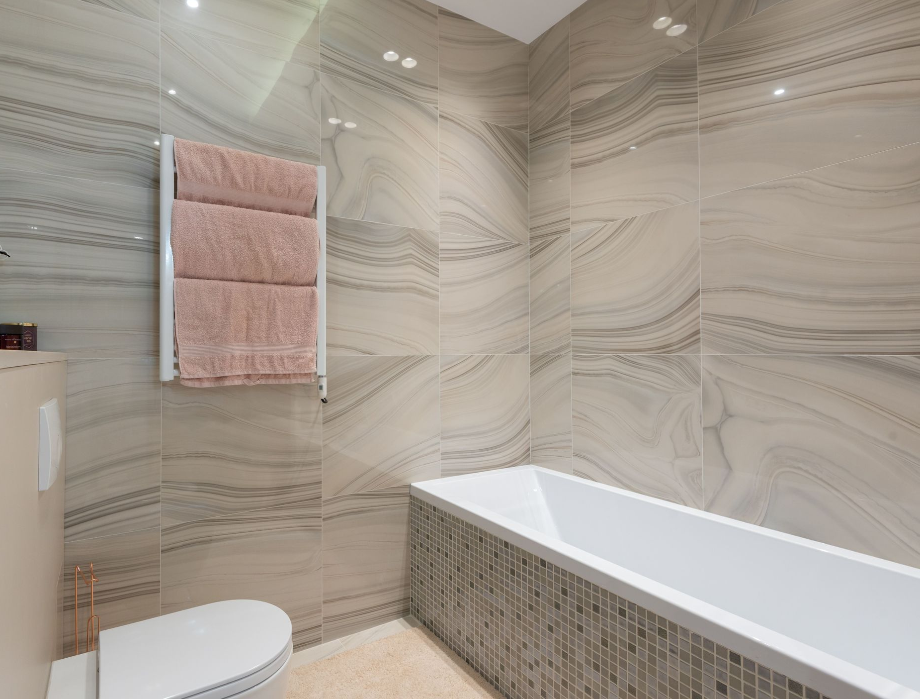 Modern bathroom with marble walls, white tub, and pink towel hanging on a rack