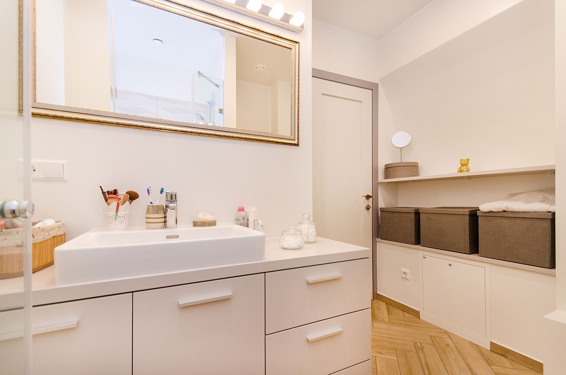 Bright modern bathroom with white vanity, gold-framed mirror, and woven storage baskets under the counter