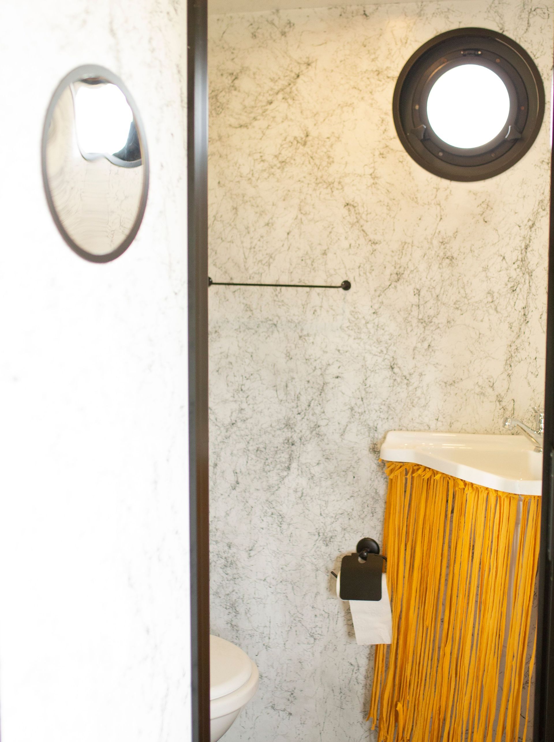 Small bathroom with textured beige walls, circular mirror, towel bar, and orange shower curtain.