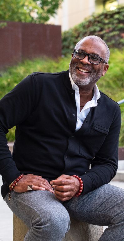 A man in a blue suit and tie is smiling with his hands folded.