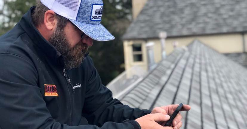 A man with a beard is using a cell phone on a roof.