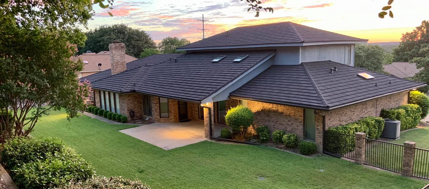 A large house with a black roof is sitting on top of a lush green hillside.