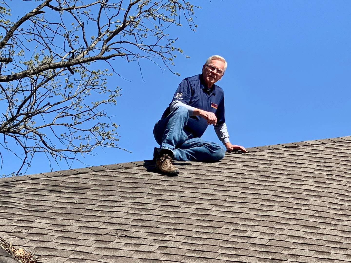 A man is sitting on top of a roof with a tree in the background.