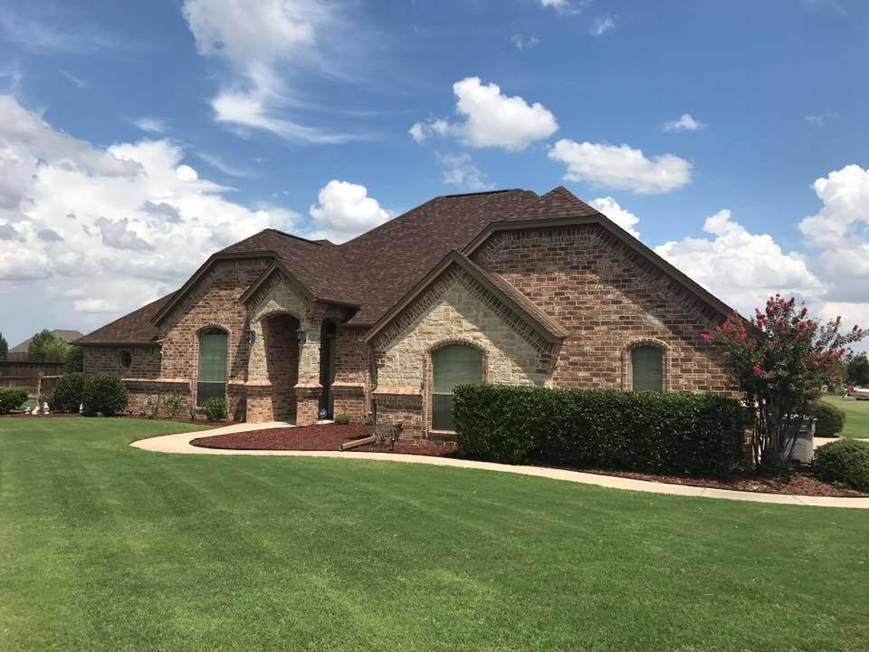 A large brick house with a brown roof is sitting on top of a lush green lawn.