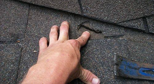 A person 's hand is reaching for a nail on a roof.