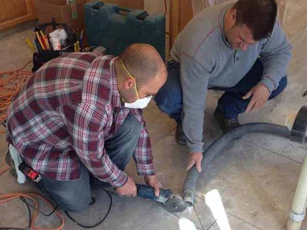Two men are kneeling on the floor using a grinder.