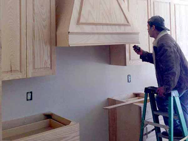 A man is standing on a ladder in a kitchen looking at a hood.