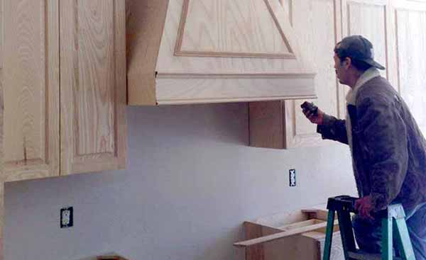 A man is standing on a ladder in a kitchen looking at a hood.