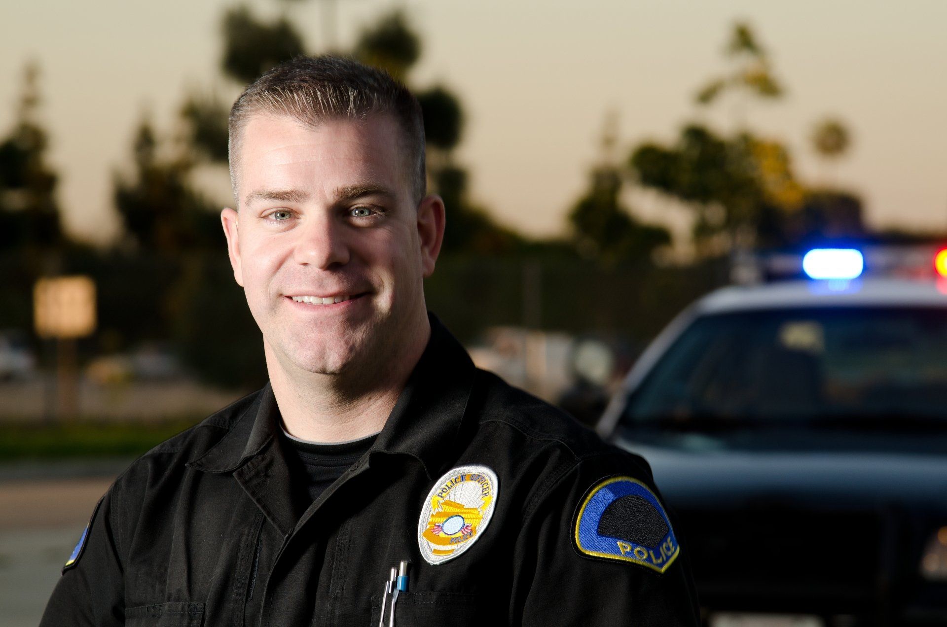 A police officer is smiling in front of a police car.