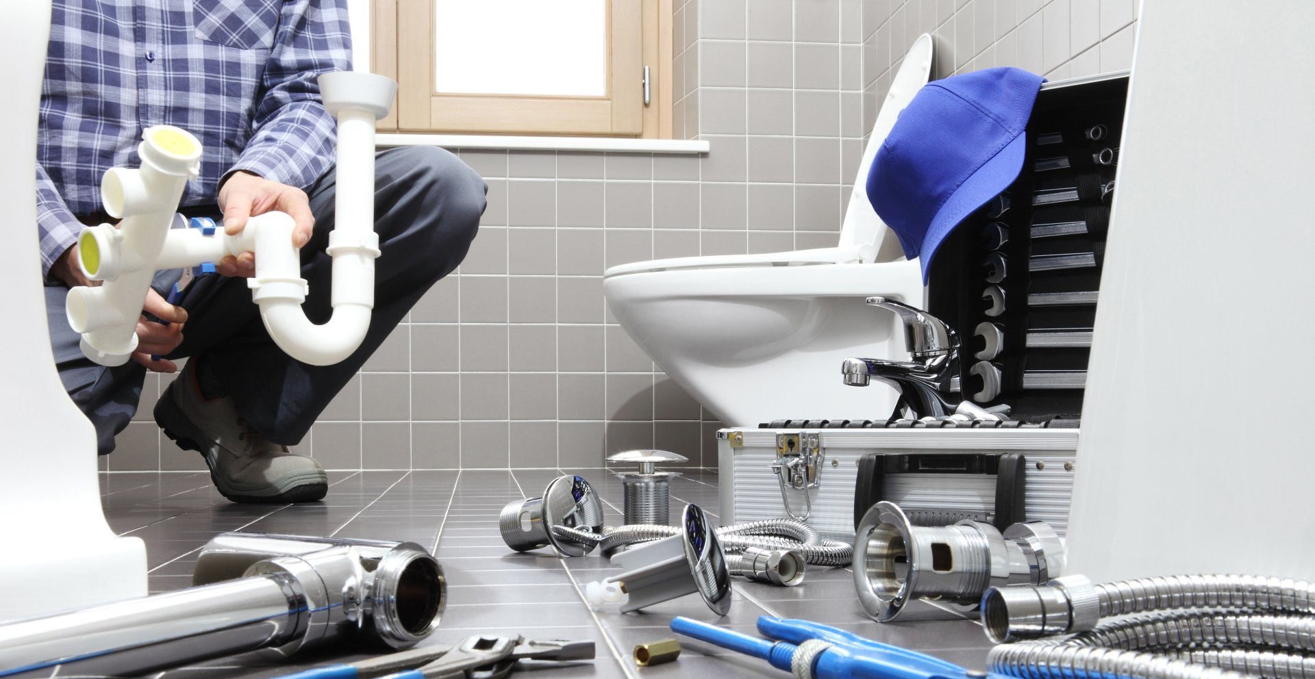 A plumber is fixing a toilet in a bathroom.