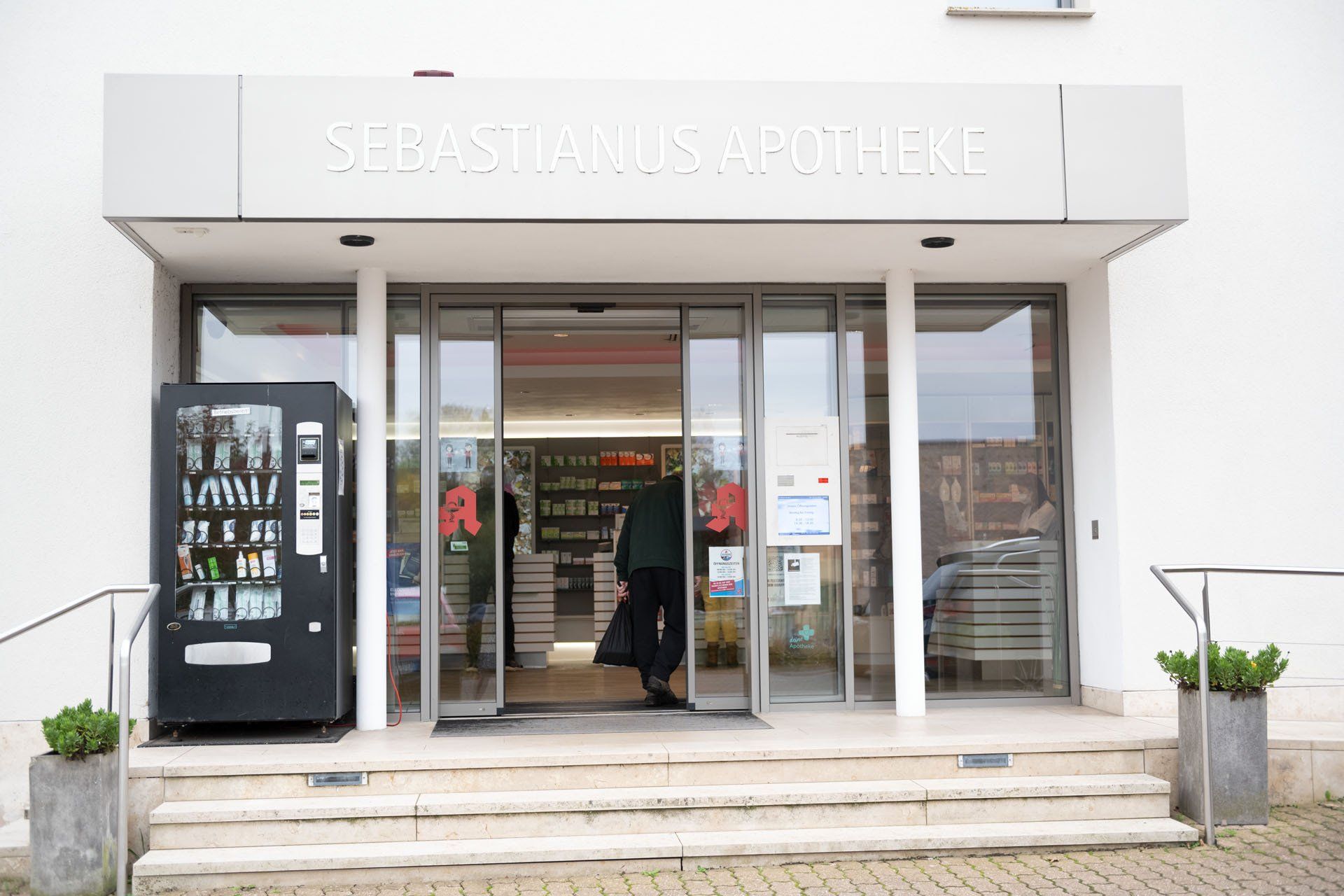 Der Eingang einer Apotheke mit einem Getränkeautomaten davor.