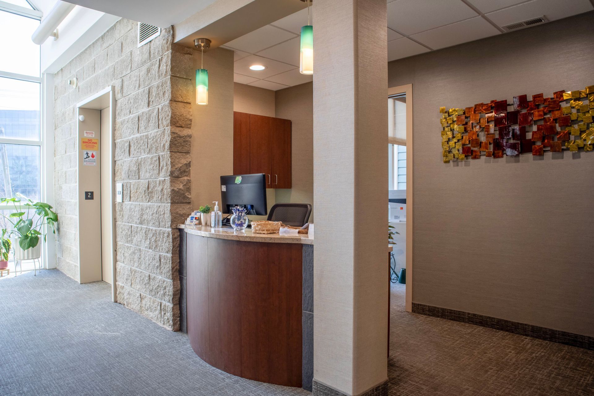 A reception desk with a computer sits in a modern office lobby with stone accents and a textured wall art installation.