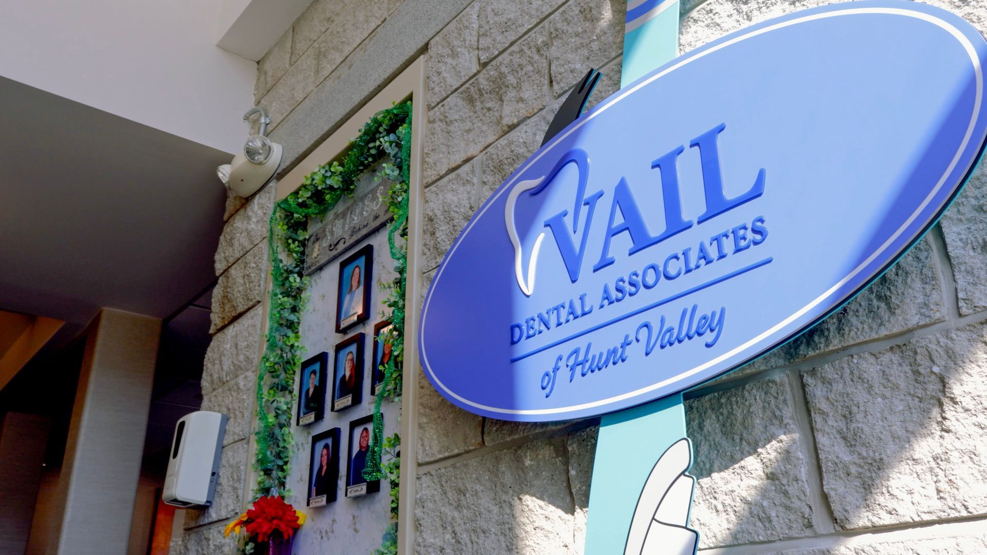 Blue oval sign for Vail Dental Associates of Hunt Valley on a stone wall next to a display of framed staff portraits.