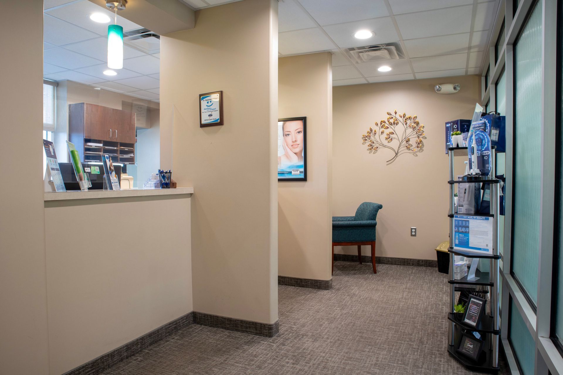 A clean waiting room with a reception desk on the left, a teal armchair, and a tiered display stand on the right.