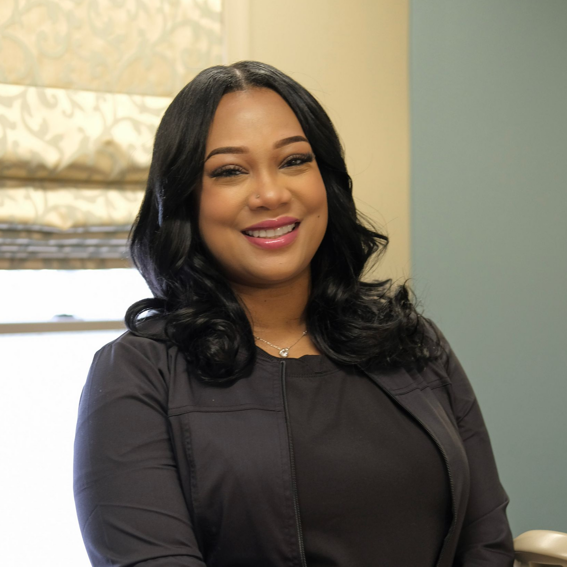 Danielle with long black hair, smiling, wearing a black shirt and silver necklace, against a blue background.