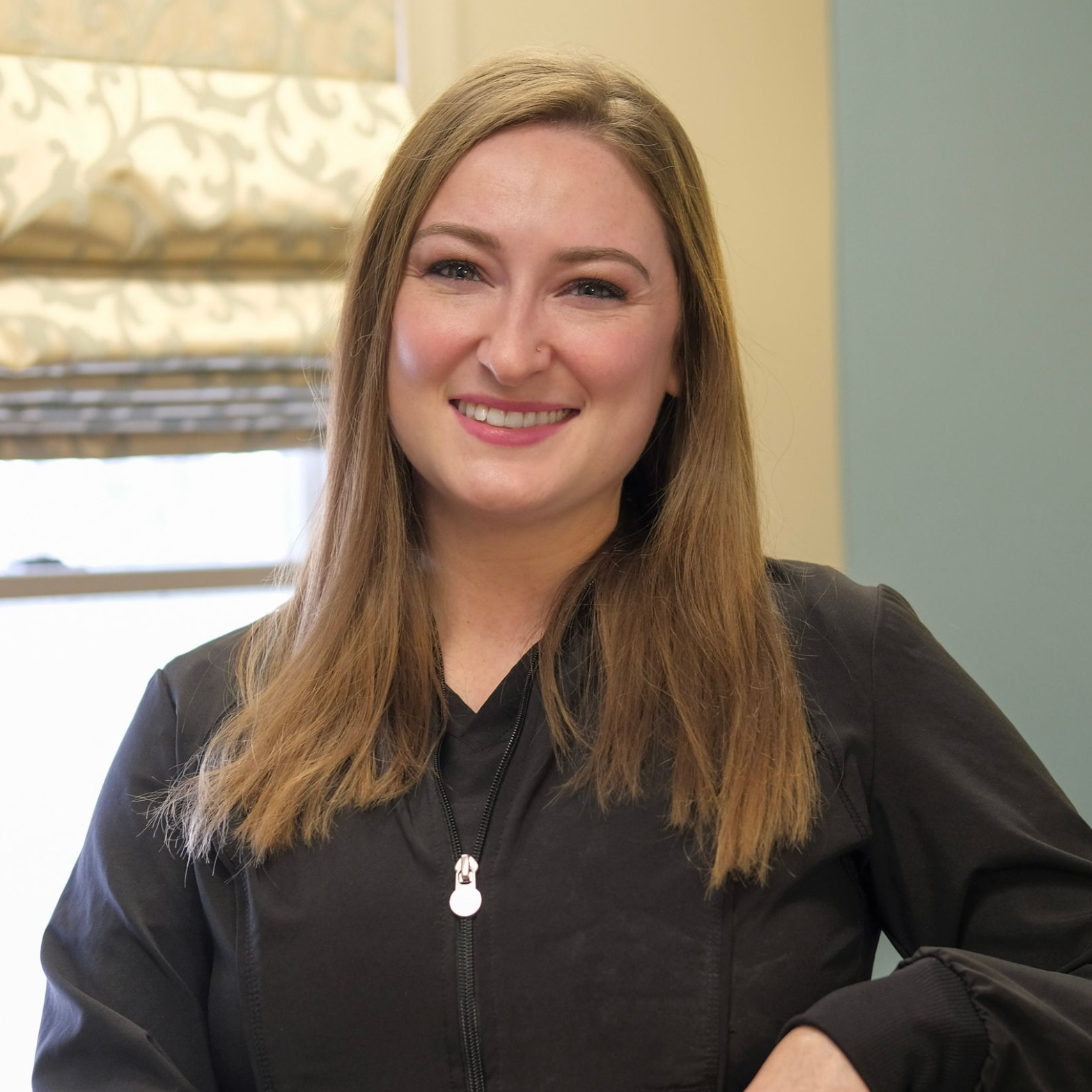 Marissa with long brown hair smiling against a blue backdrop. She is wearing a black shirt.