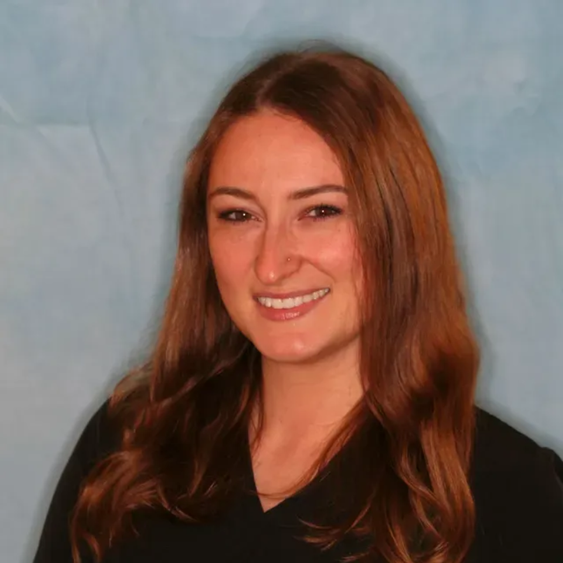 Marissa with long brown hair smiling against a blue backdrop. She is wearing a black shirt.