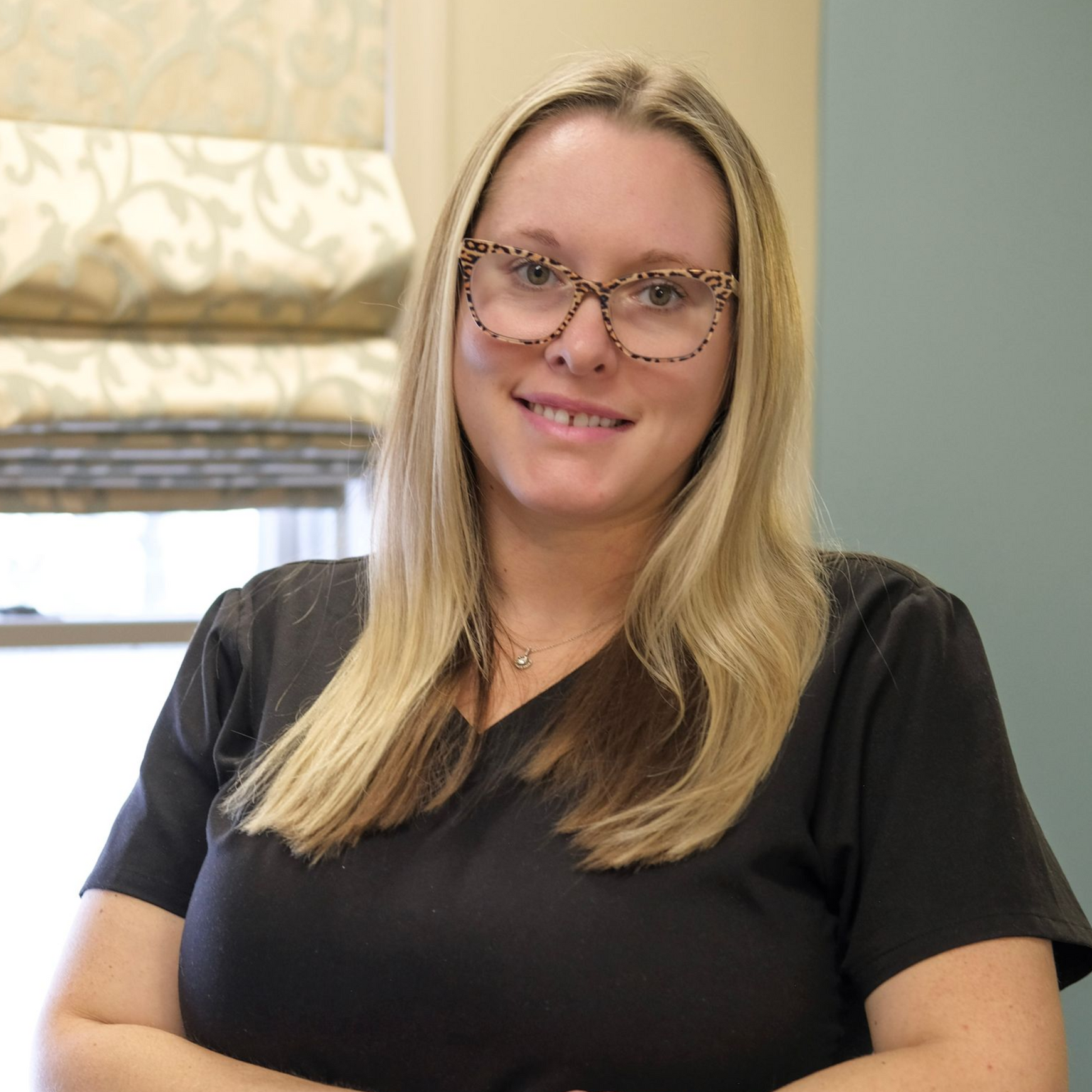 Danielle with long black hair, smiling, wearing a black shirt and silver necklace, against a blue background.