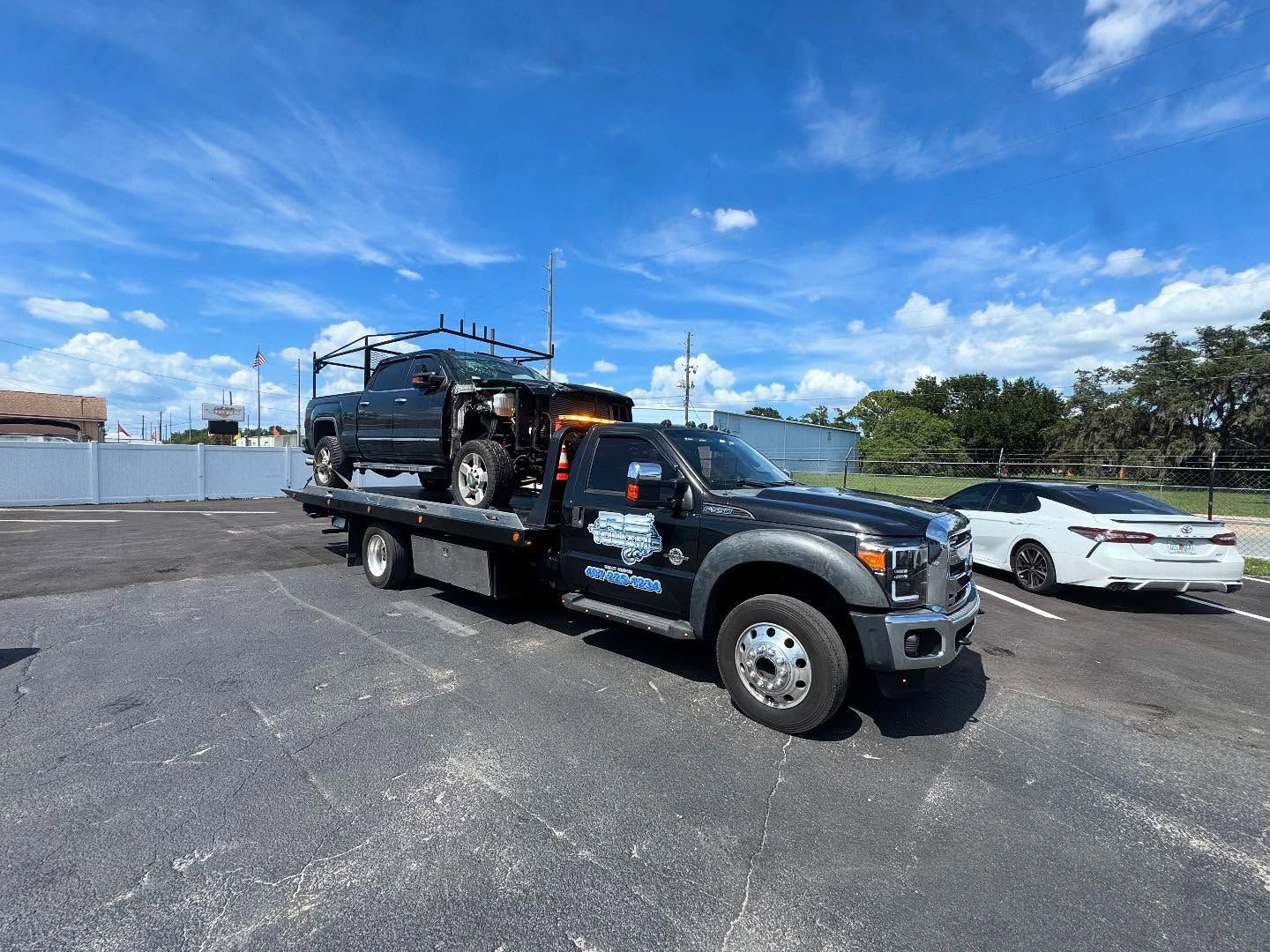 A tow truck is carrying a car on the back of it in a parking lot.