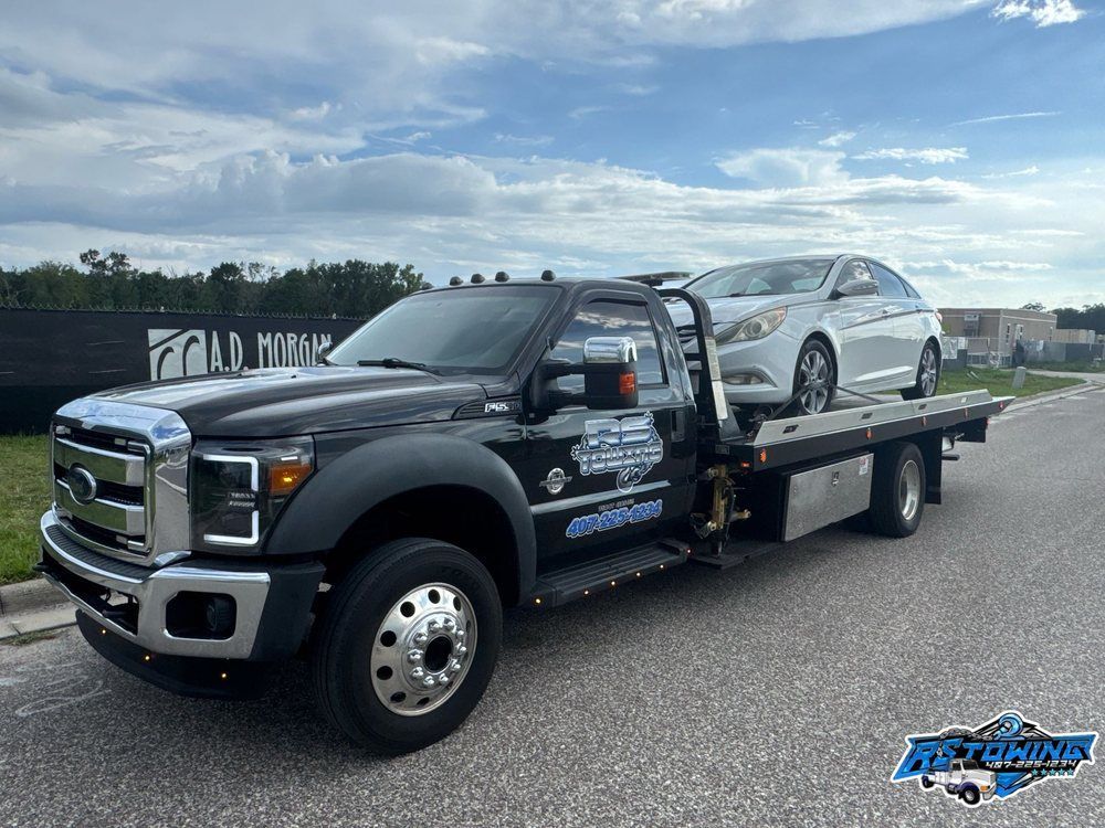 A tow truck with a car on the back is parked on the side of the road.