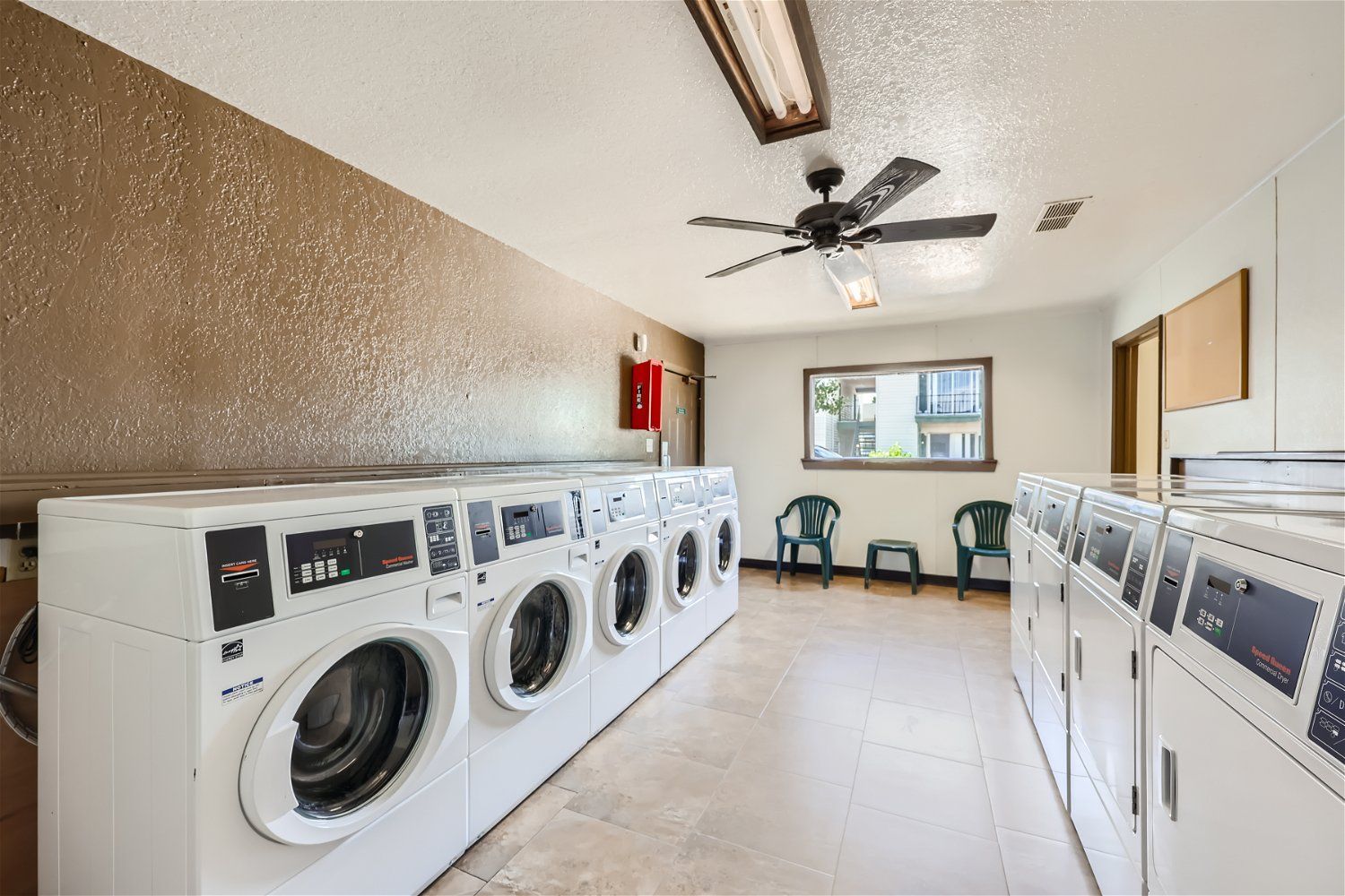 Check out our apartments for rent in Elk City, OK, at Crestview Commons.  These are the resident laundry facilities, with rows of washers and dryers, a ceiling fan, and a small window.