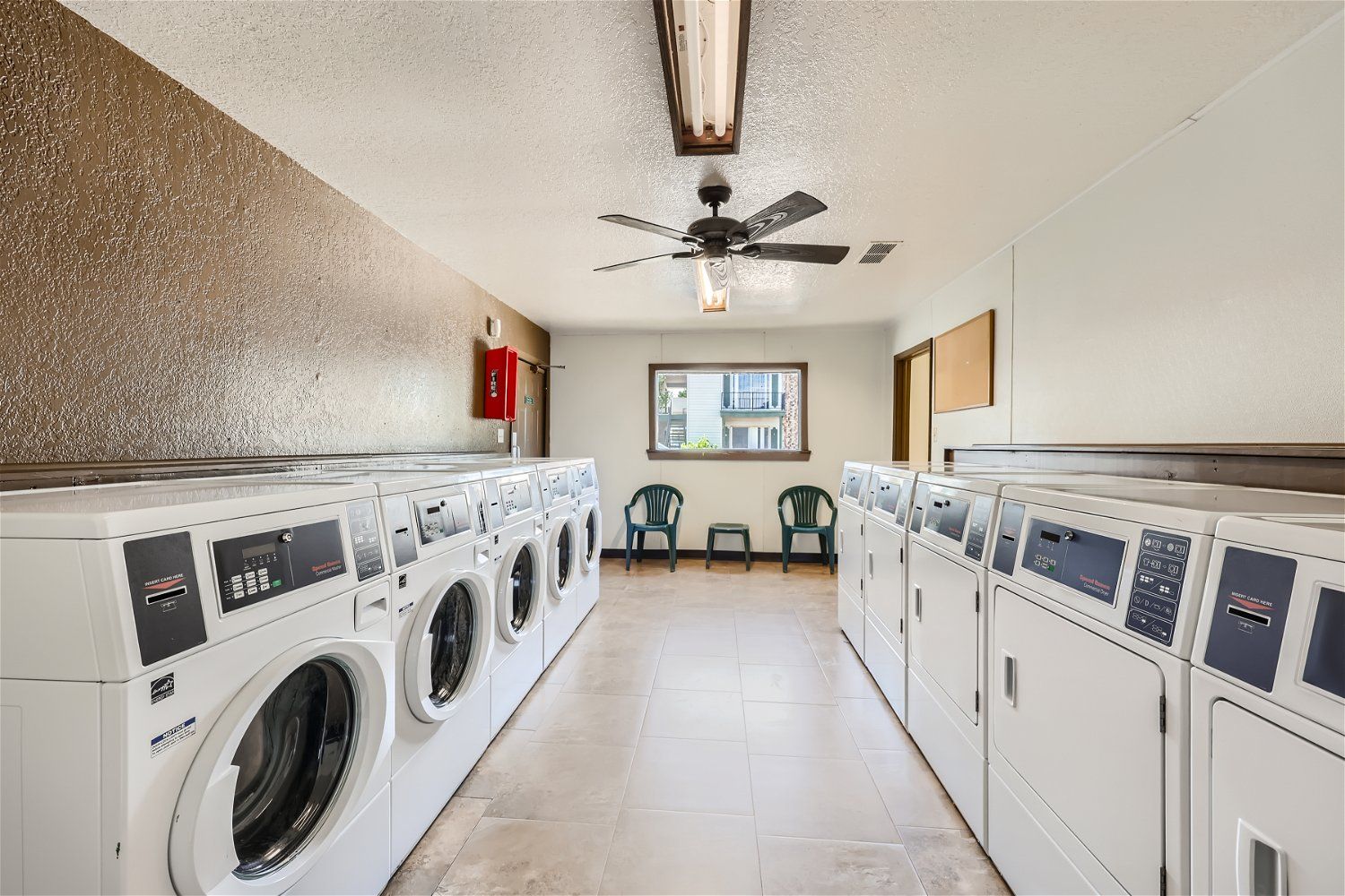 Check out our apartments for rent in Elk City, OK, at Crestview Commons.  These are the resident laundry facilities, with rows of washers and dryers, a ceiling fan, and a small window.