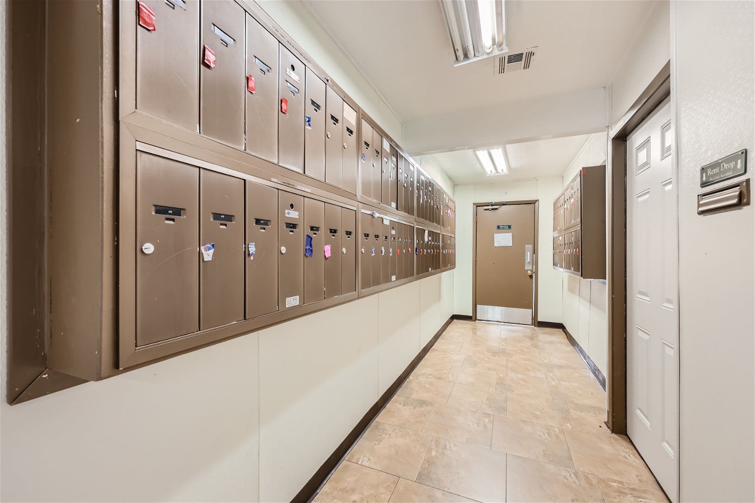 Check out our apartments for rent in Elk City, OK, at Crestview Commons.  These are the resident mailboxes. This hallway shows rows of mailboxes on both sides; a door is open in the middle, and another room is visible at the end.