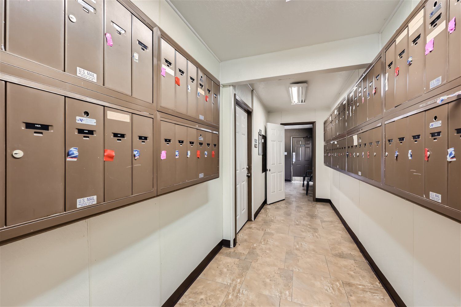 Check out our apartments for rent in Elk City, OK, at Crestview Commons.  These are the resident mailboxes. This hallway shows rows of mailboxes on both sides; a door is open in the middle, and another room is visible at the end.
