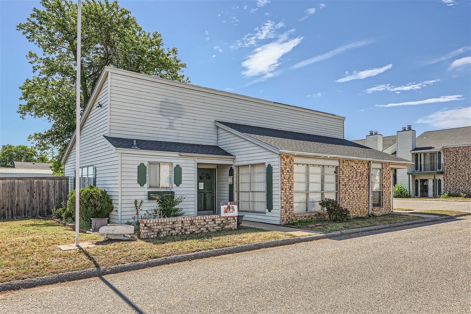 Check out our apartments for rent in Elk City, OK, at Crestview Commons.  This is an exterior view of an apartment building. The parking lot is visible, there are green trees in the background, and a bright blue sky with white clouds.
