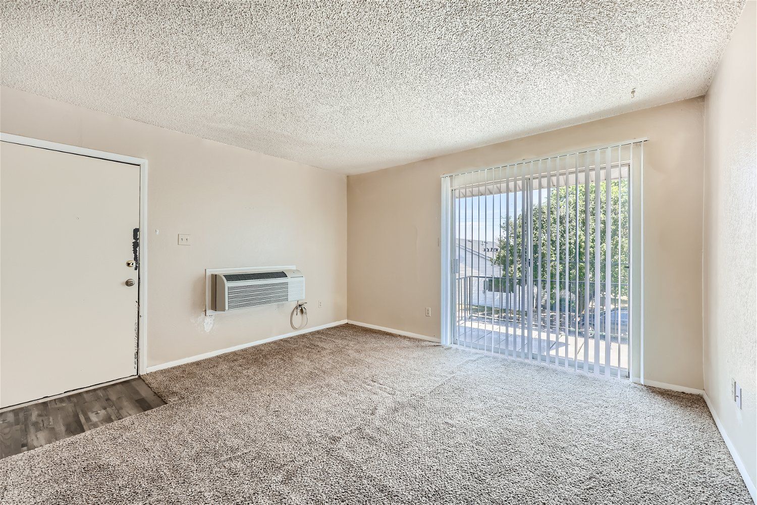 Check out our apartments for rent in Elk City, OK, at Crestview Commons.  This living room has carpet, a sliding glass door, and a wall-mounted AC unit.