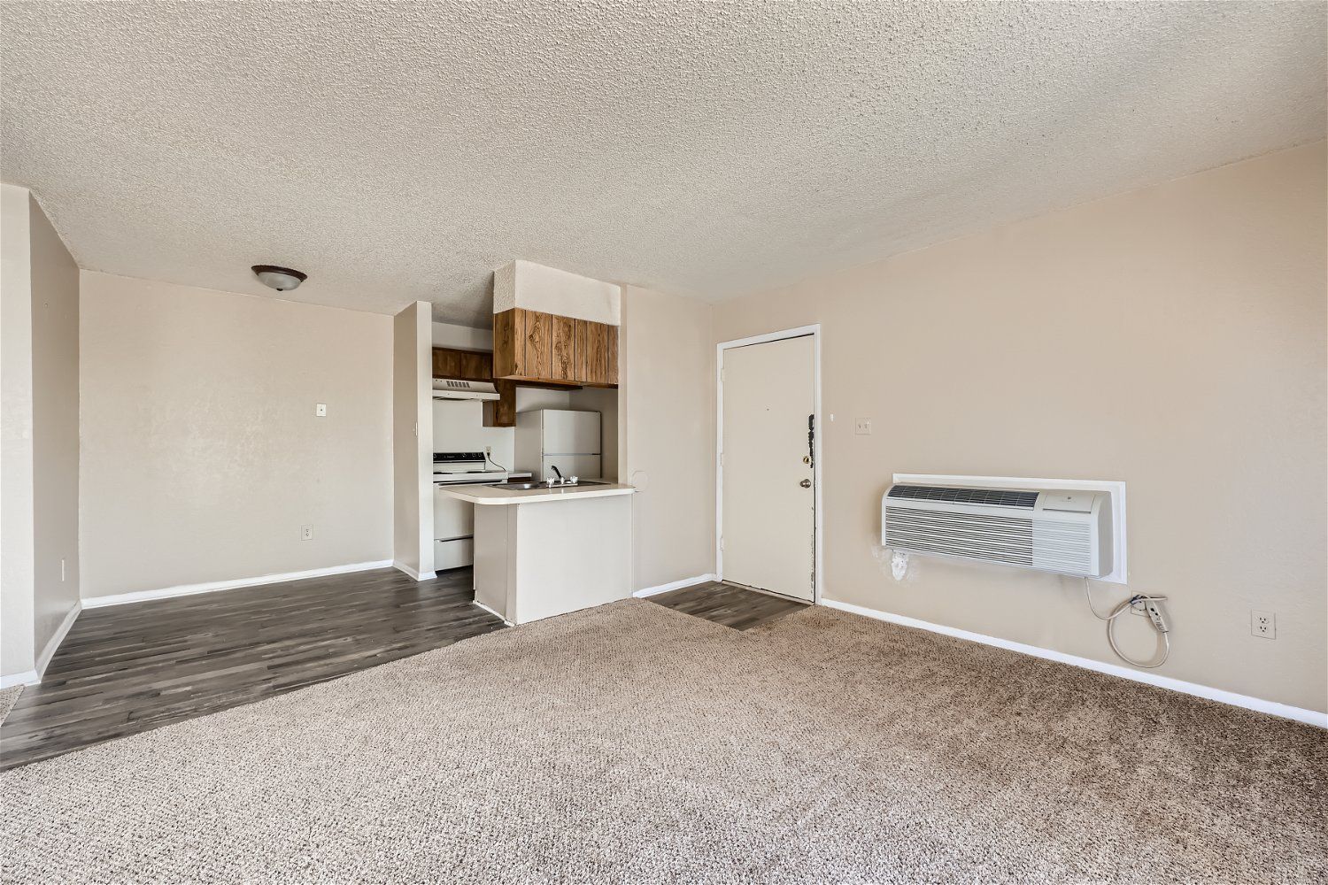 Check out our apartments for rent in Elk City, OK, at Crestview Commons. This is an interior of an apartment with a kitchen, a living area with carpet, and an air conditioning unit.