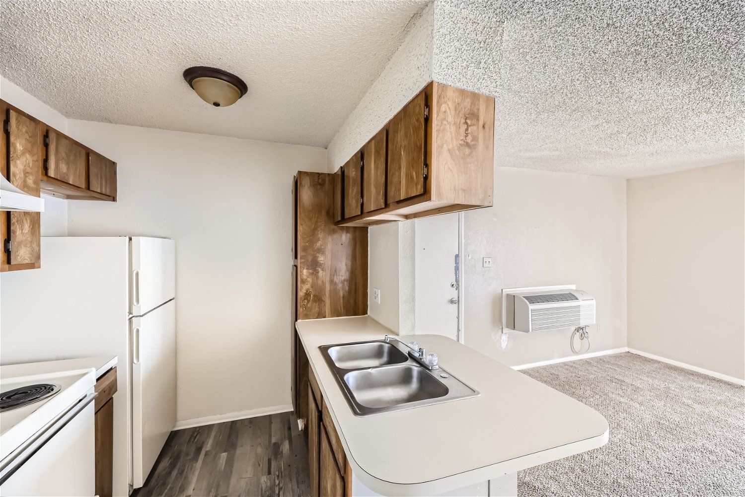 Check out our apartments for rent in Elk City, OK, at Crestview Commons. This apartment kitchen features wood cabinets, white appliances, a countertop with a sink, and a wood-like floor.