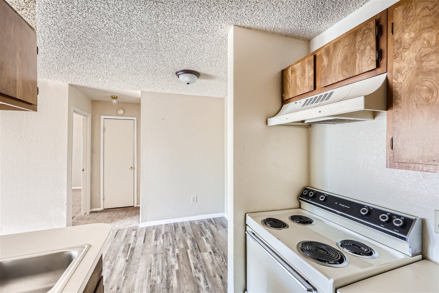 Check out our apartments for rent in Elk City, OK, at Crestview Commons.  This kitchen comes with a white stove, wooden cabinets, and a hallway in the background.