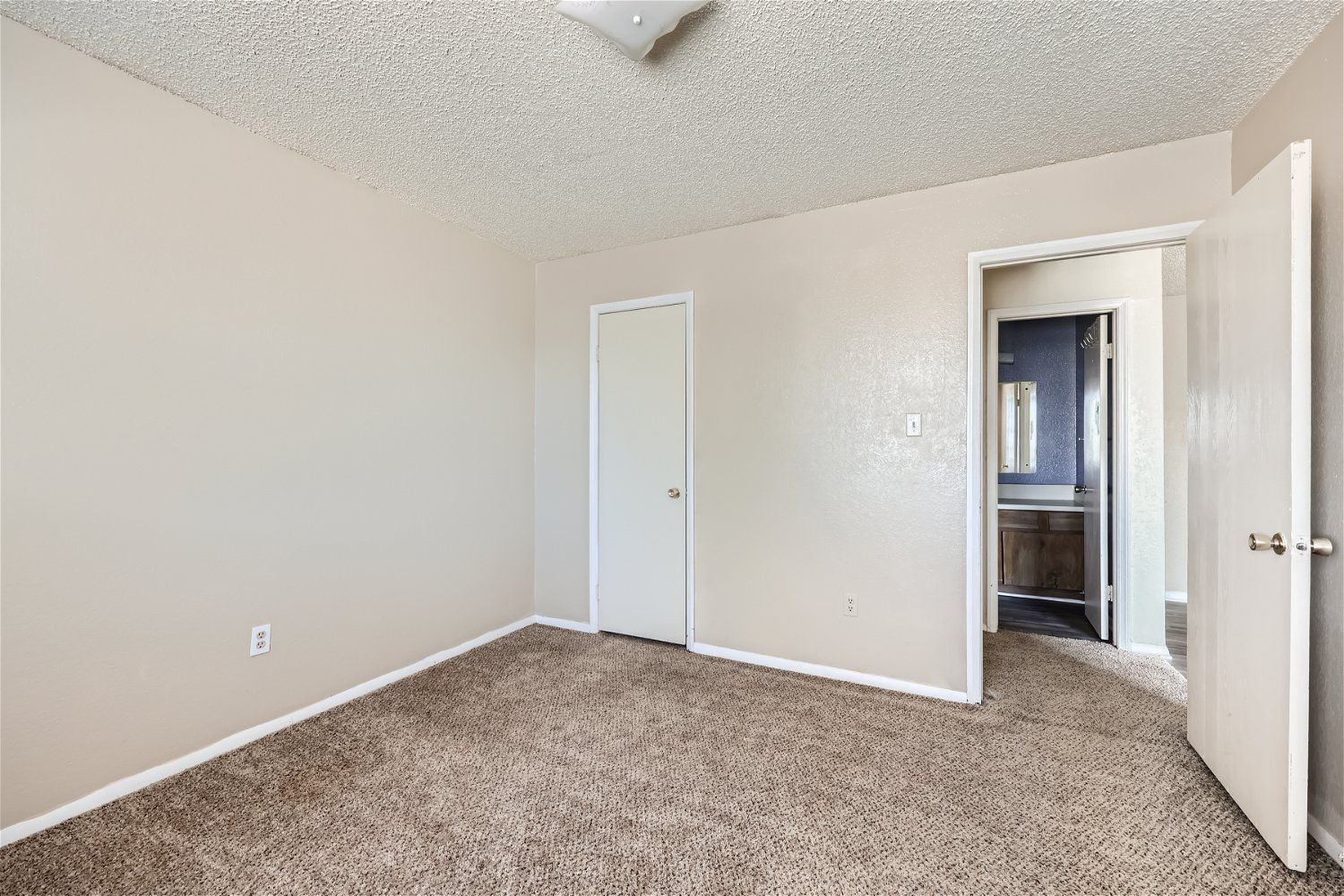Check out our apartments for rent in Elk City, OK, at Crestview Commons.  This bedroom has beige walls, carpet, a door to the bathroom, and a closed door.
