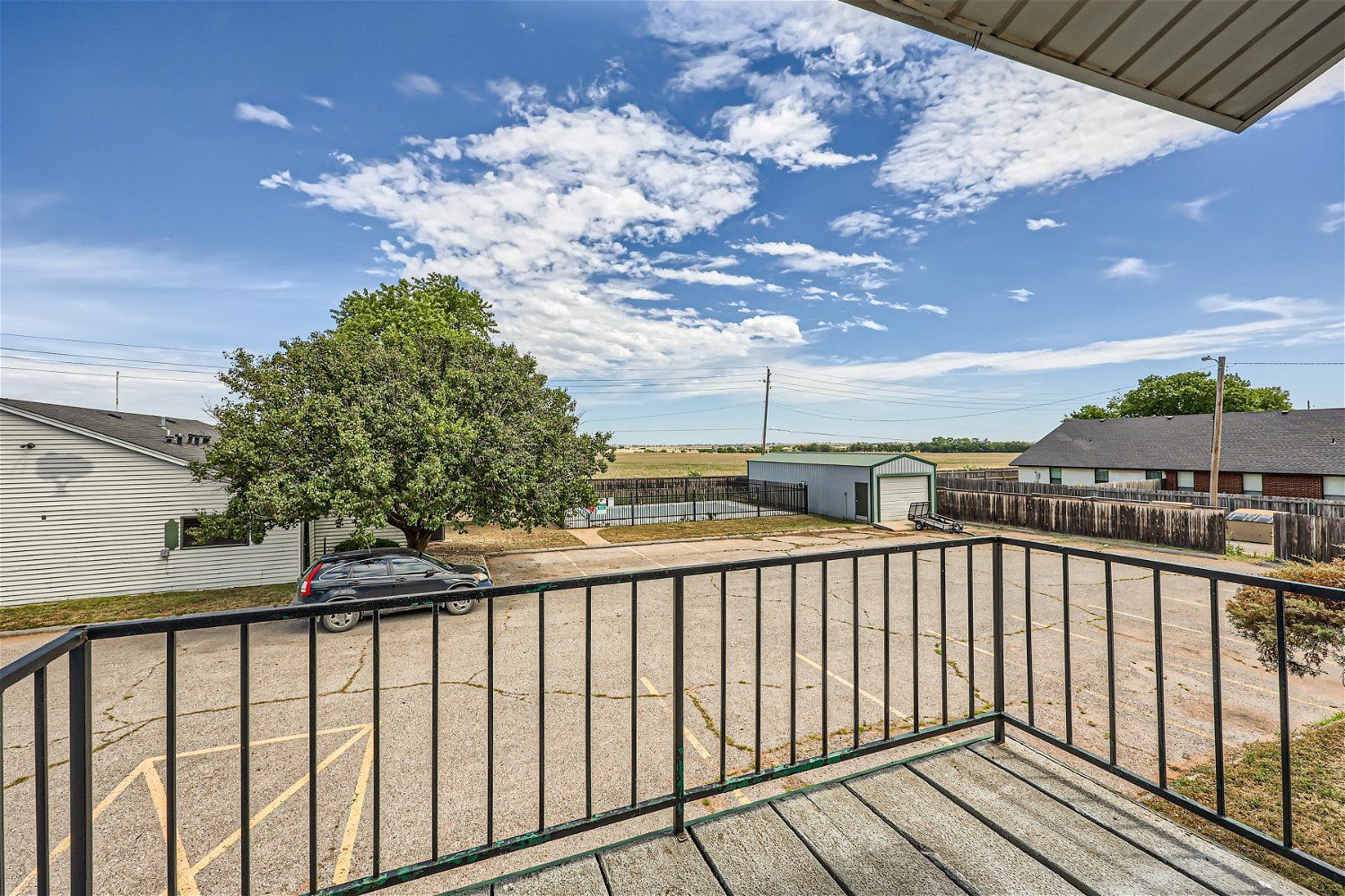 Balcony view of parking lot, tree, buildings, and blue sky with clouds.