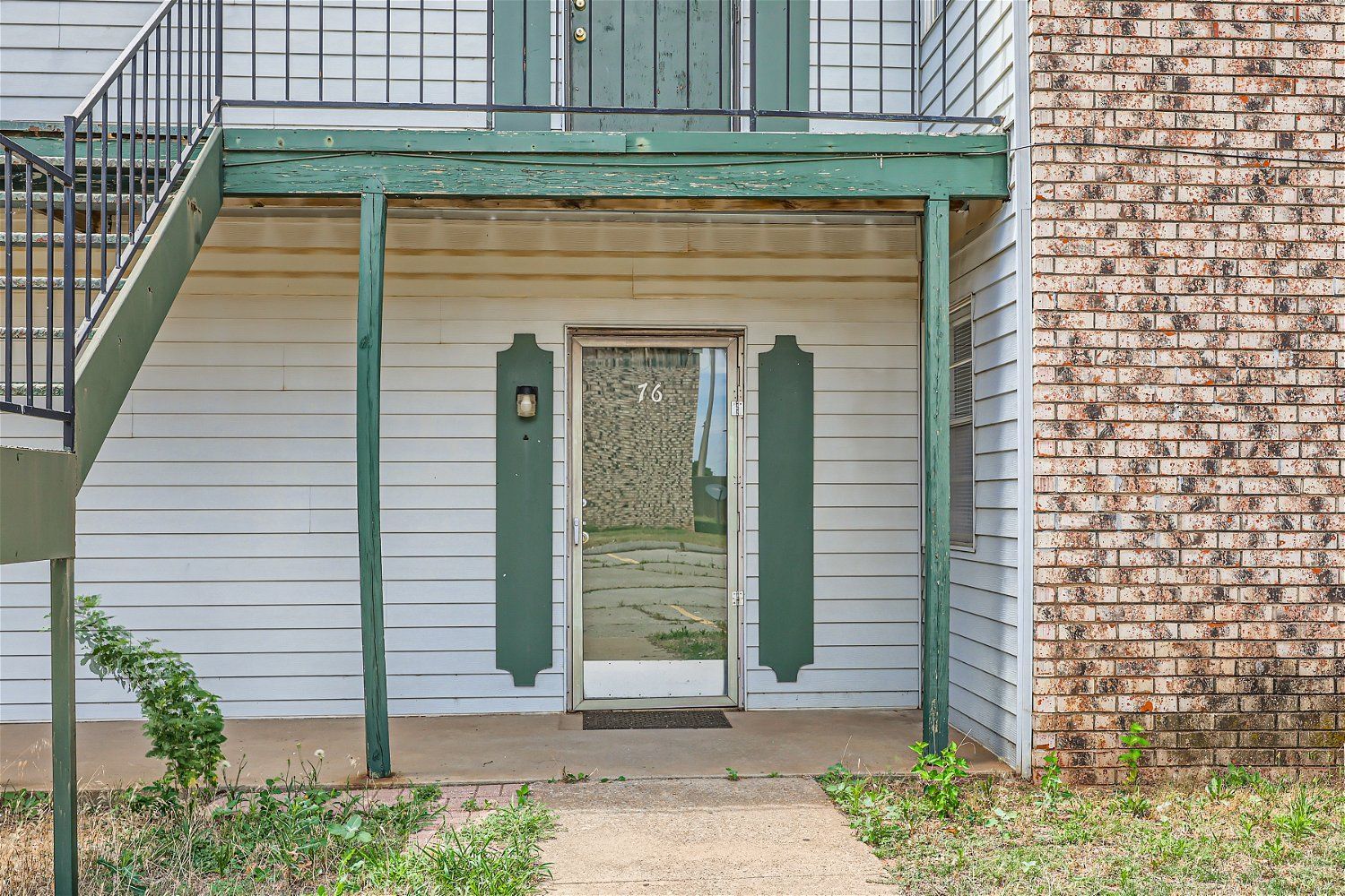 Check out our apartments for rent in Elk City, OK, at Crestview Commons.  This is an apartment exterior of a building with a white facade, green trim, and a door, with an exterior staircase on the left.