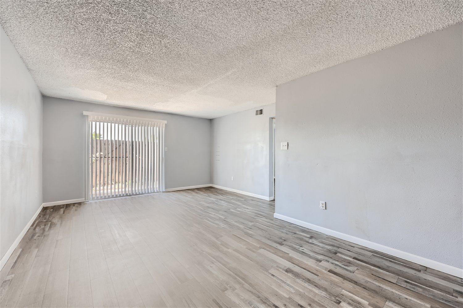 Check out our apartments for rent in Elk City, OK, at Crestview Commons. This apartment living room has wood-look flooring, light gray walls, a sliding glass door, and a popcorn ceiling.