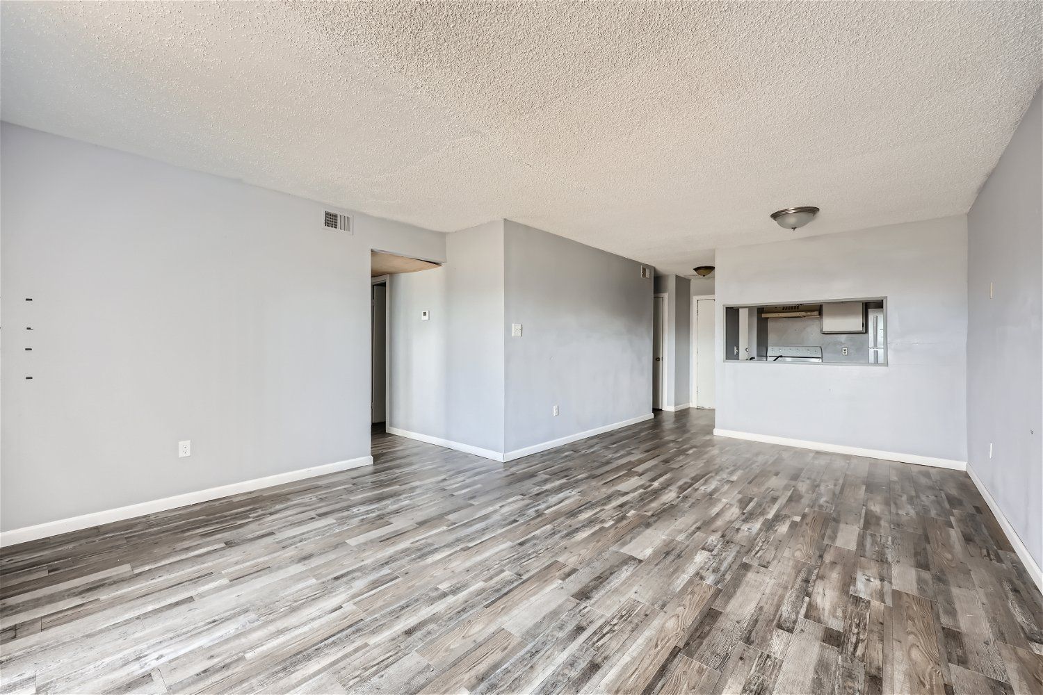 Check out our apartments for rent in Elk City, OK, at Crestview Commons. This apartment interior has gray walls, wood-look flooring, and a pass-through to the kitchen.