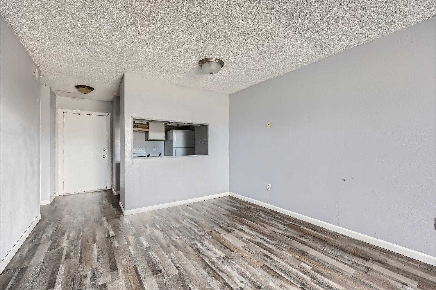 Check out our apartments for rent in Elk City, OK, at Crestview Commons. This apartment interior has gray walls, wood-look flooring, and a small pass-through to the kitchen.