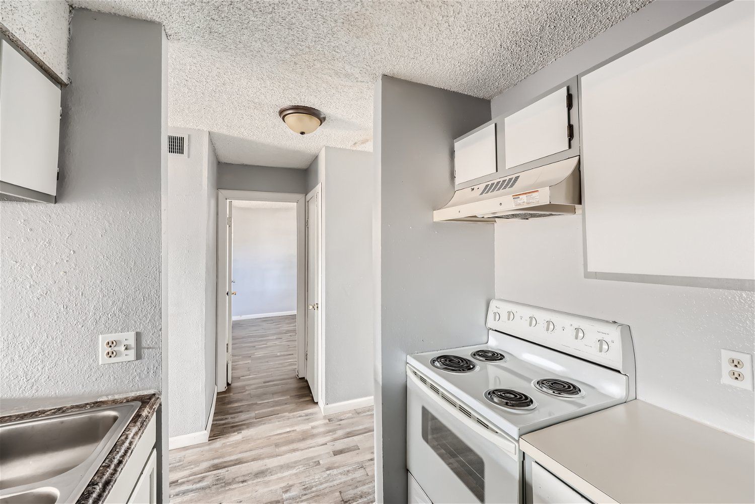 Check out our apartments for rent in Elk City, OK, at Crestview Commons. This kitchen features white appliances, gray walls, and a view into a hallway.