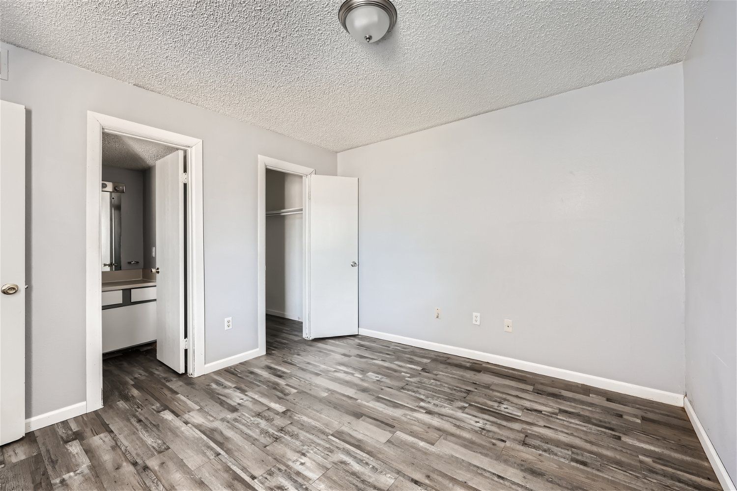 Empty room with light gray walls, wood-look floor, and doors.