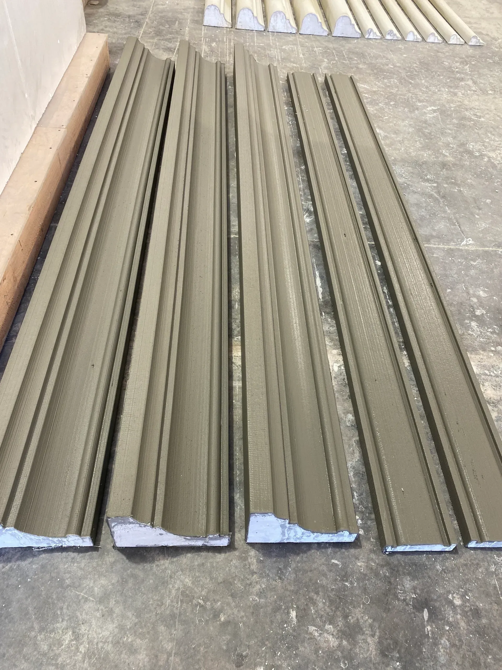 Stacked gray metal trim pieces on a concrete floor in a workshop or construction area