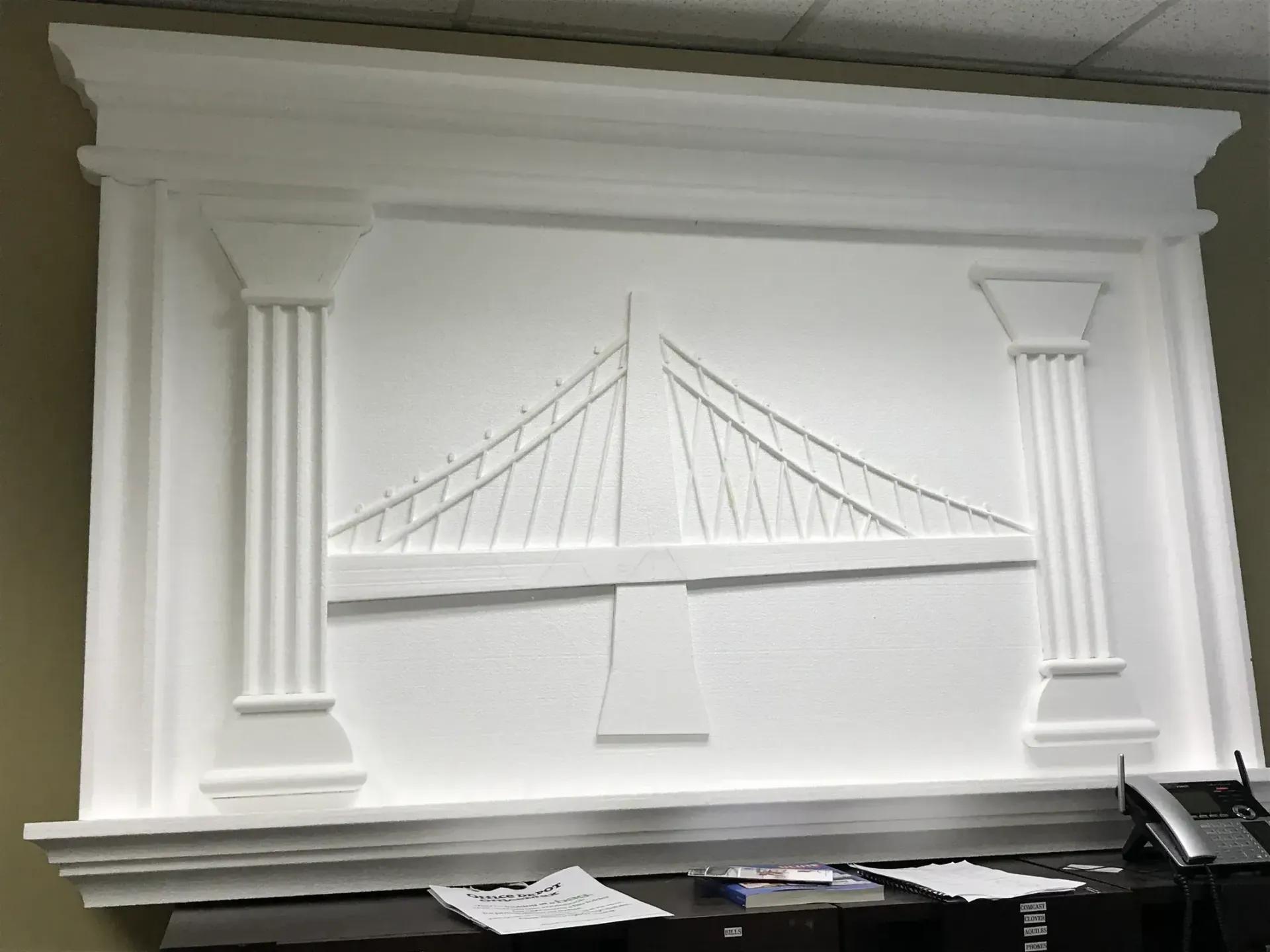 White decorative wall panel with a relief of a suspension bridge and classical columns, above a keyboard.