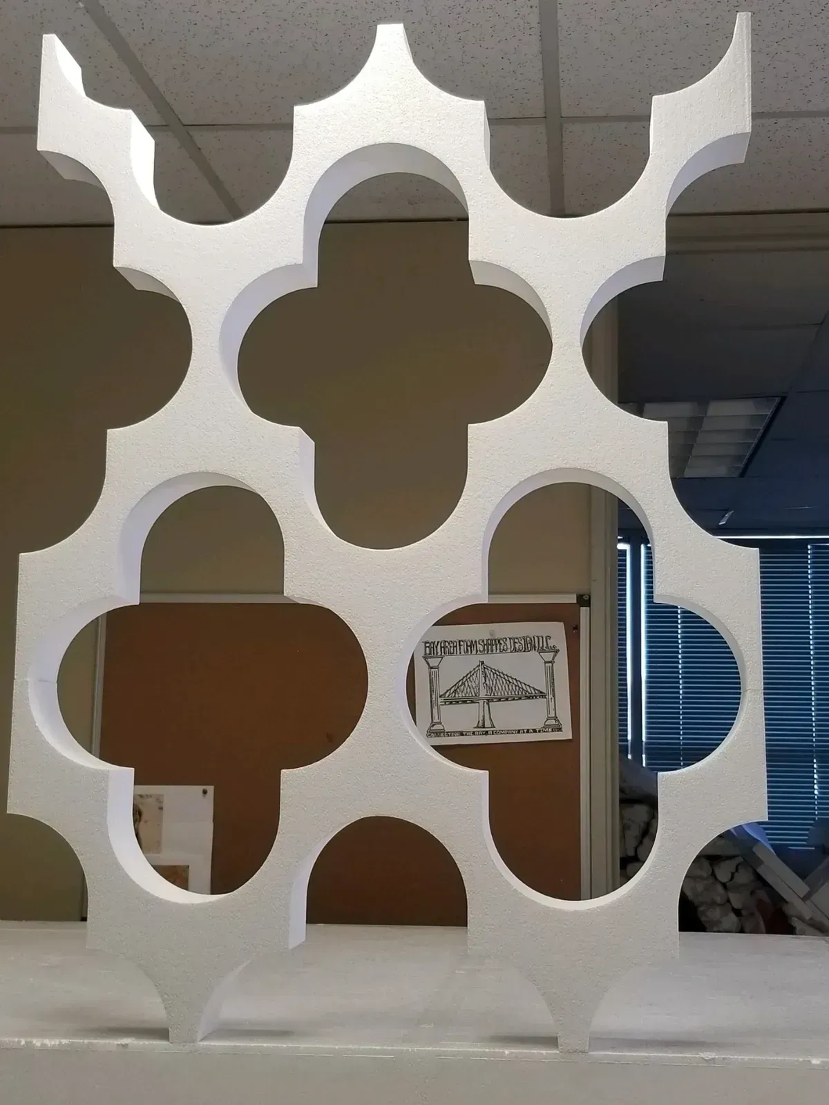 White decorative partition with quatrefoil cutouts in an office or lobby area, with a sign behind it
