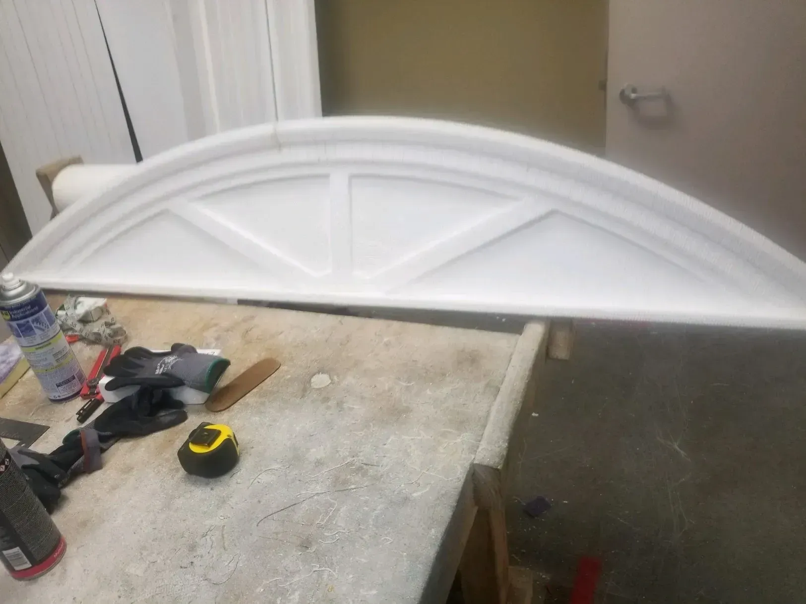 White arched decorative panel leaning on a workbench in a workshop, with tools scattered nearby