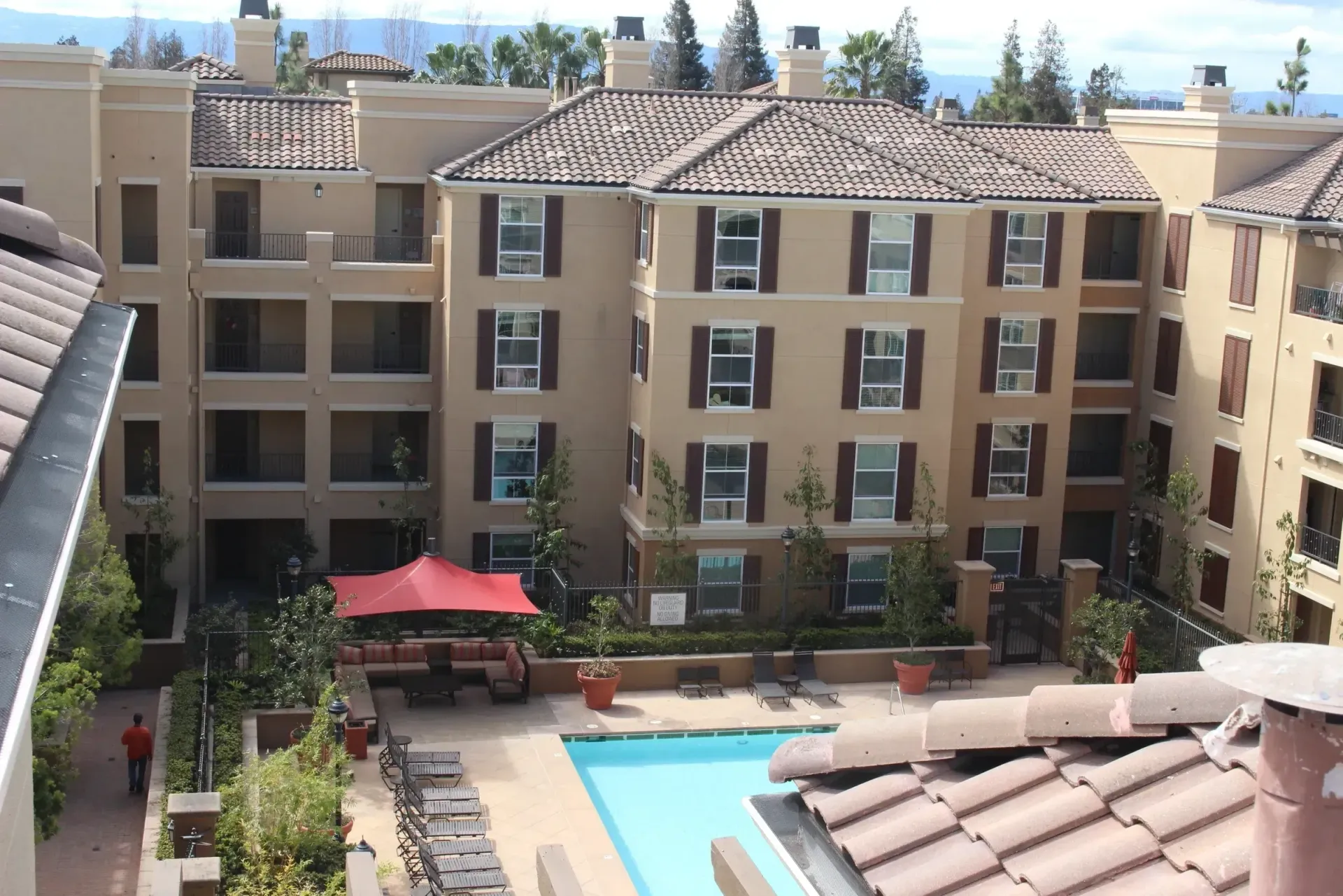 Courtyard of apartment buildings with a swimming pool and red umbrellas under a bright sky